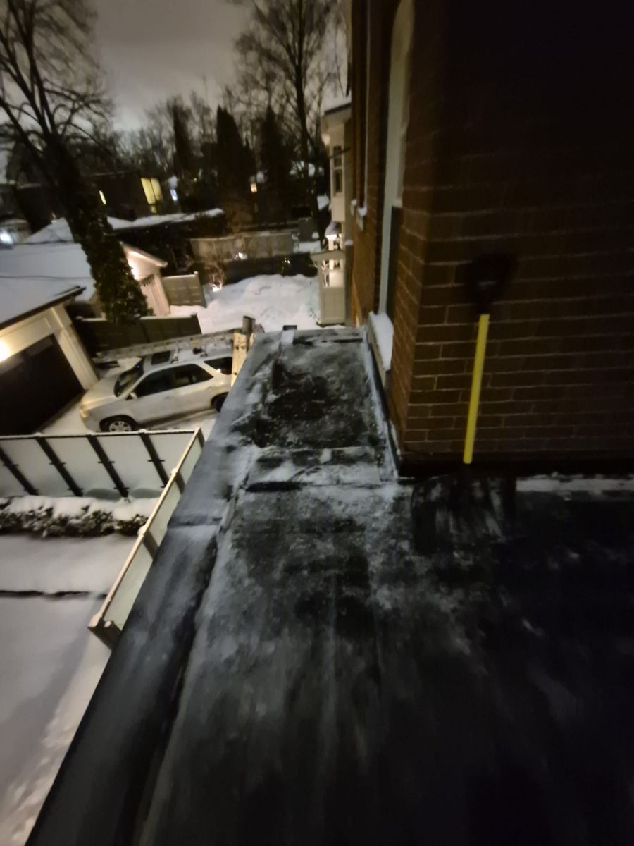 Snow shovel resting on a narrow roof ledge beside a brick wall
